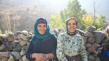 two women sitting on a rock wall